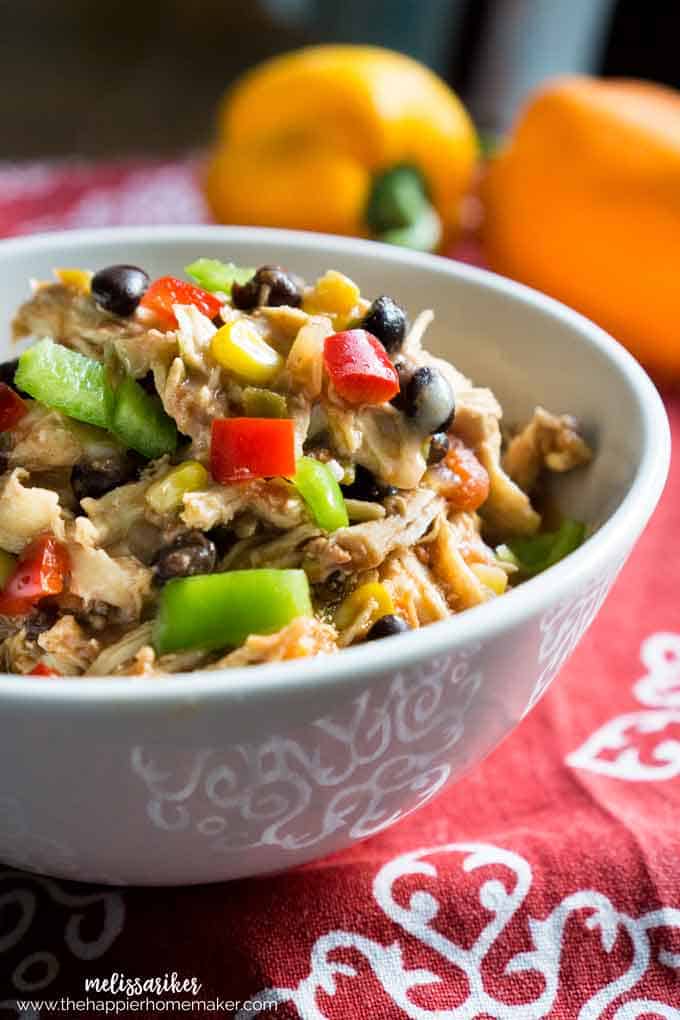 A white bowl of slow cooker Mexican chicken topped with red and green peppers 