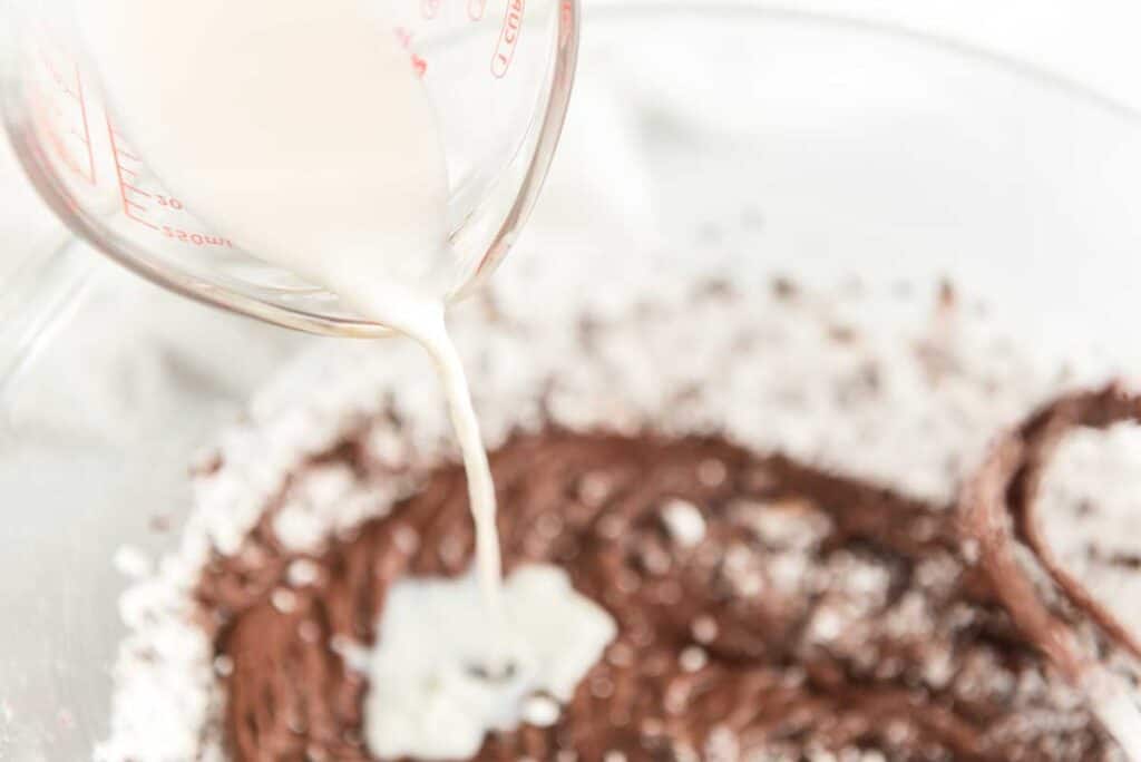 pouring milk in chocolate frosting ingredients in glass bowl