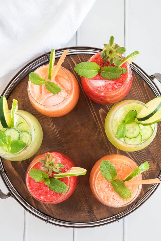 overhead view of many flavors of agua fresca in glasses on wood tray