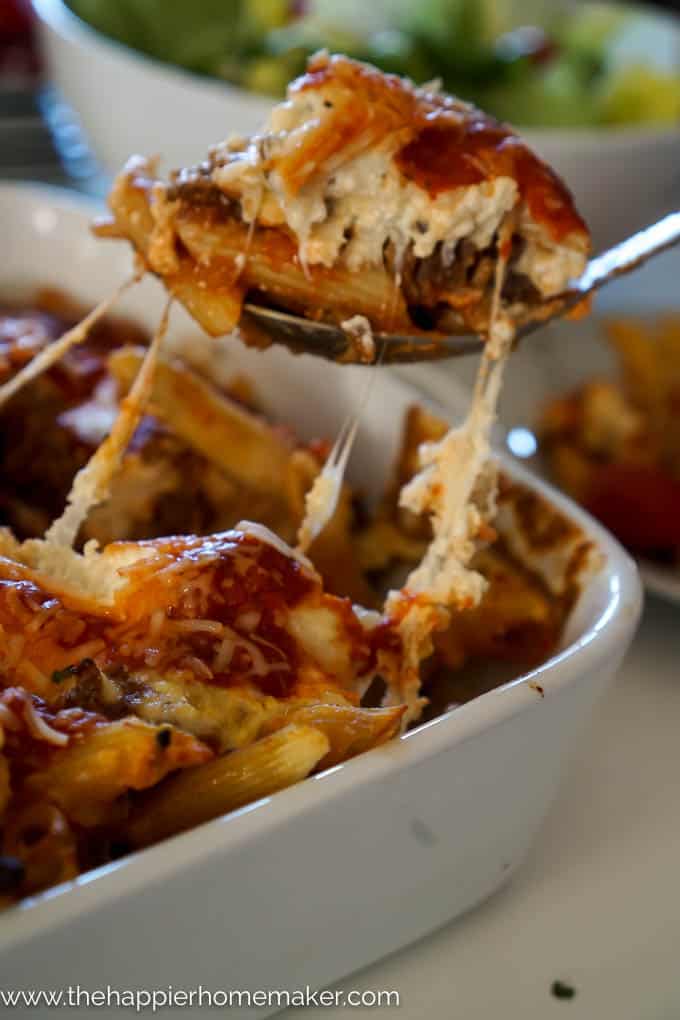 A close up of baked penne rigate in a white baking dish after cooking with a spoonful being taken away