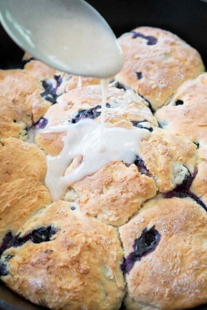 pouring lemon glaze over blueberry buttermilk biscuits