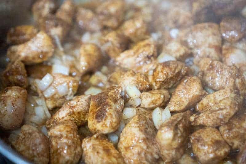 chicken breast cut into pieces with cajun seasoning in pan