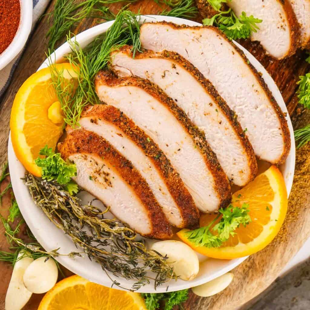 sliced cajun smoked turkey breast on plate with orange slices and herbs