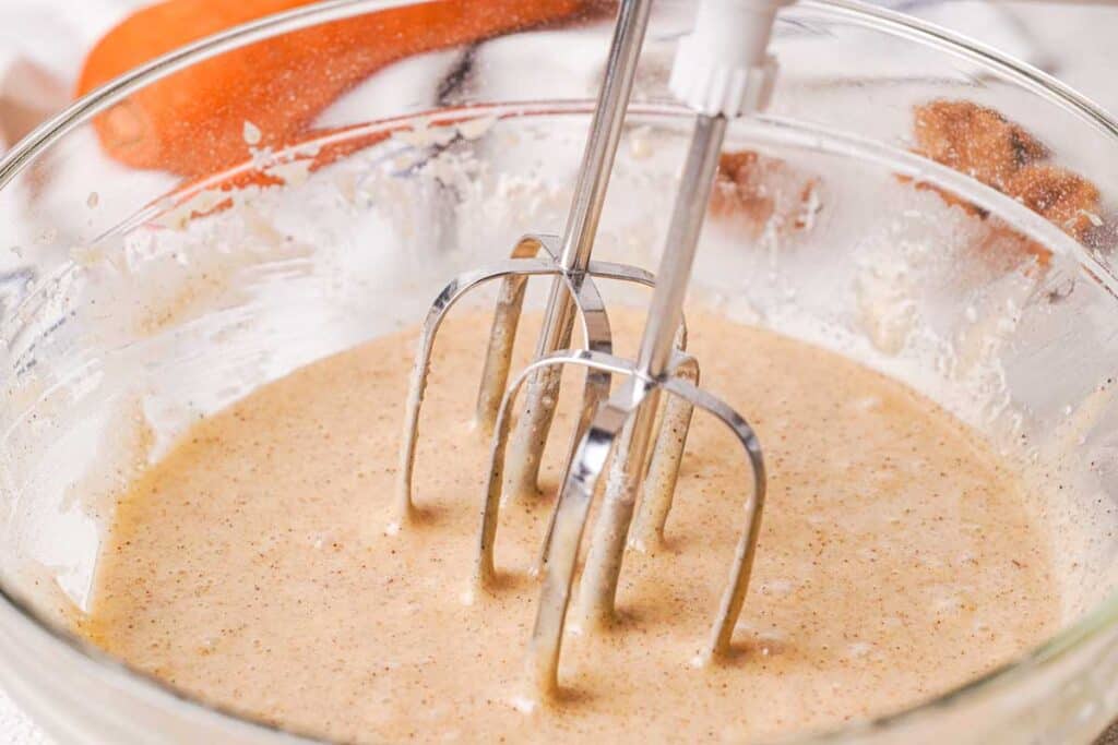mixer in glass bowl of carrot cake muffin batter