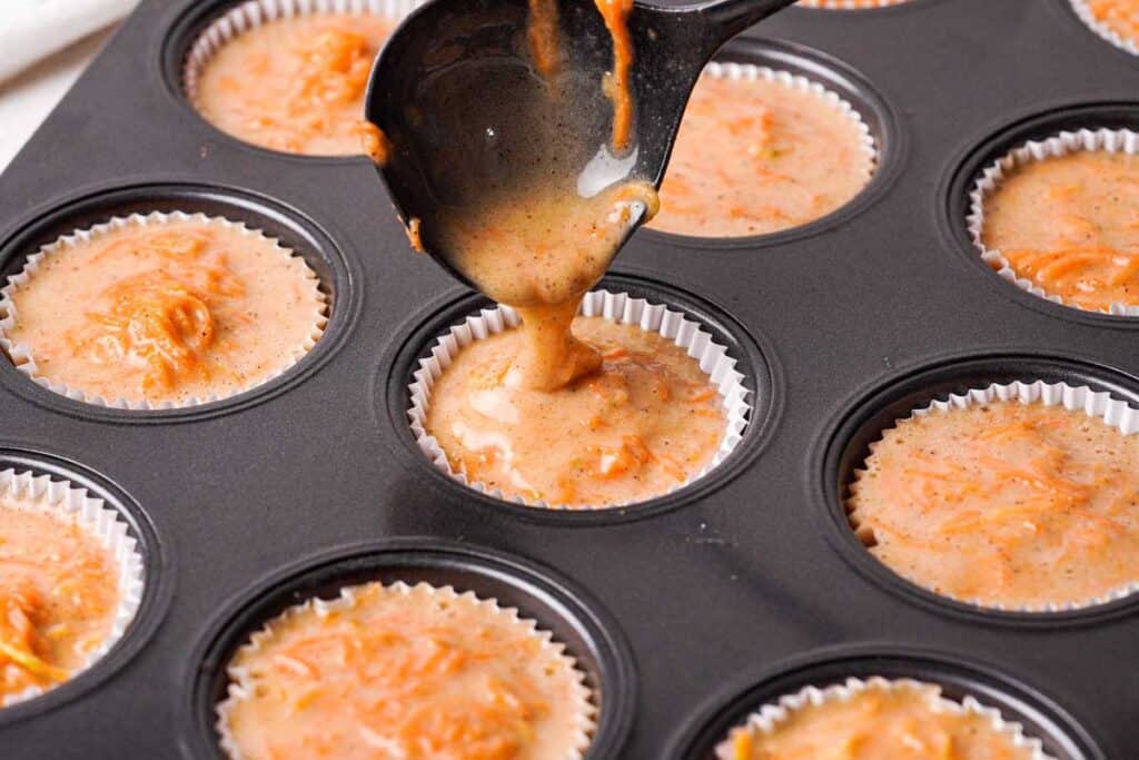 spoon pouring carrot cake muffin batter into cupcake pan
