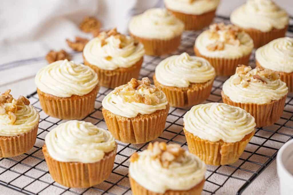 carrot cake muffins on wire rack with cream cheese frosting and some have chopped walnuts