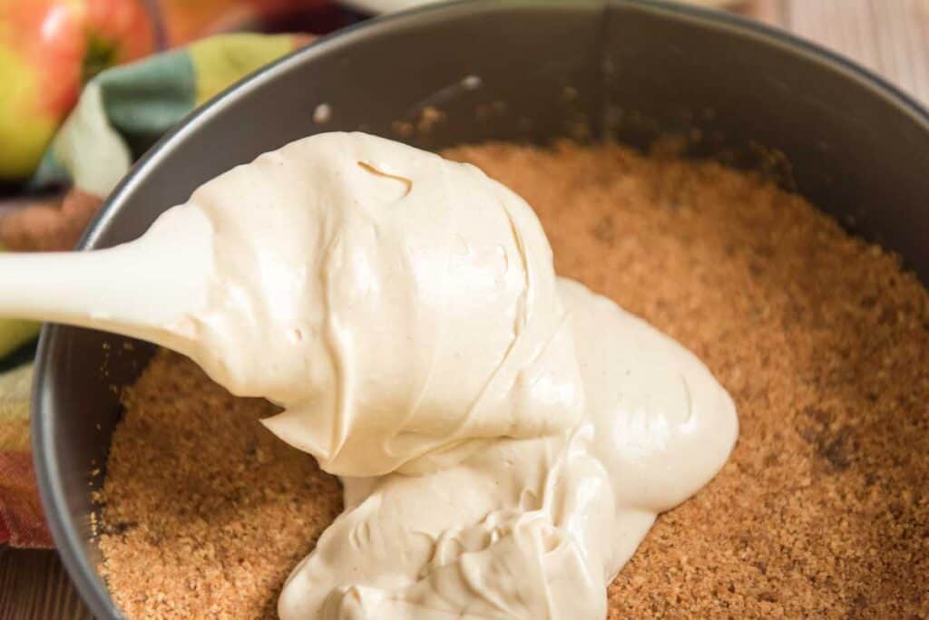 spatula adding cheesecake filling to pan with graham cracker crust