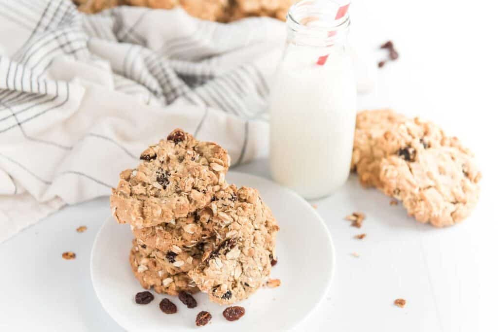 oatmeal raisin cookies on white plate with glass of milk and tea towel in background