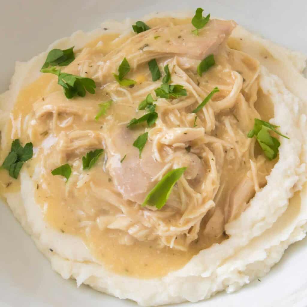 Instant Pot chicken and gravy over mashed potatoes in white bowl