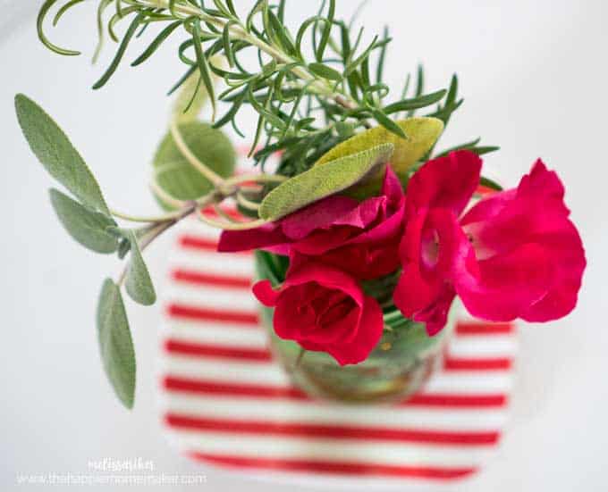 overhead view of red roses and rosemary in mason jar vase sitting on red and white striped plate