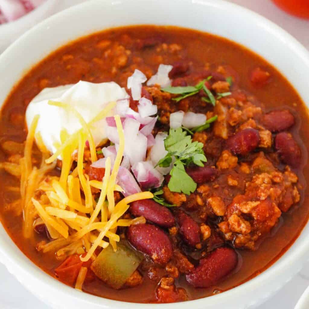 white bowl with slow cooker turkey chili topped with sour cream and cheese