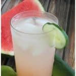 A close up of watermelon cucumber vodka cocktail garnished with a slice of cucumber with a slice of watermelon in the background