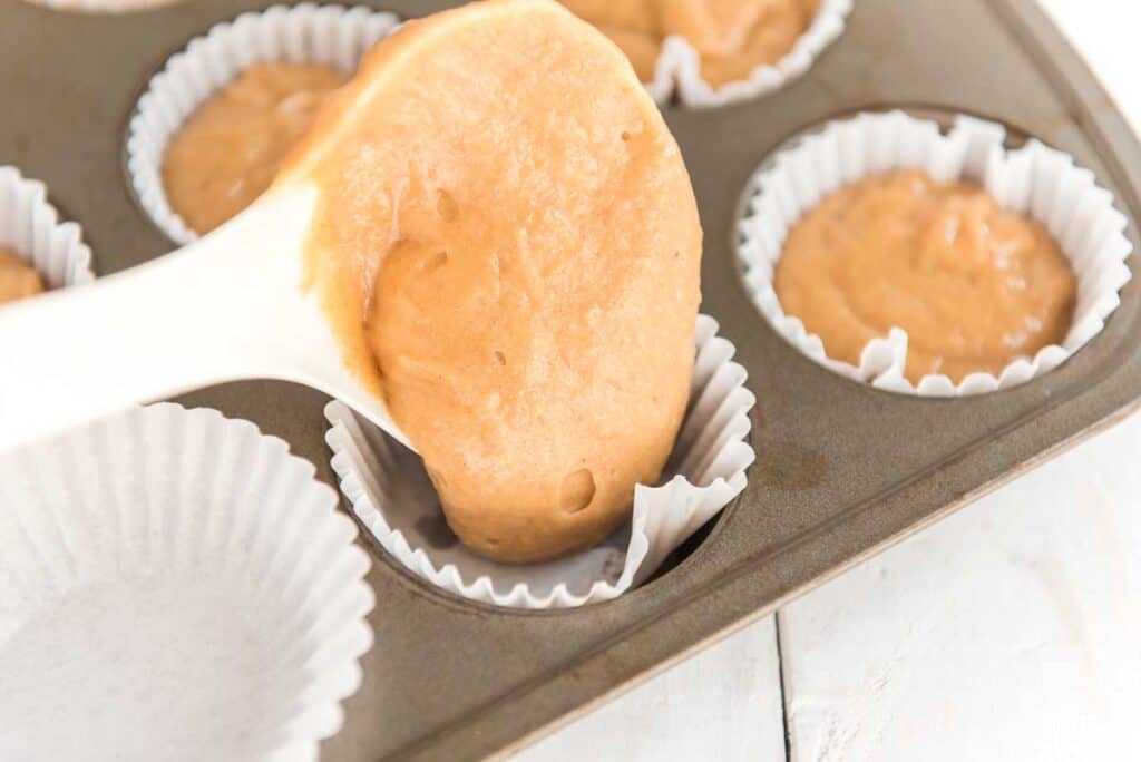 spooning peanut butter cupcake batter into muffin pan with white liners