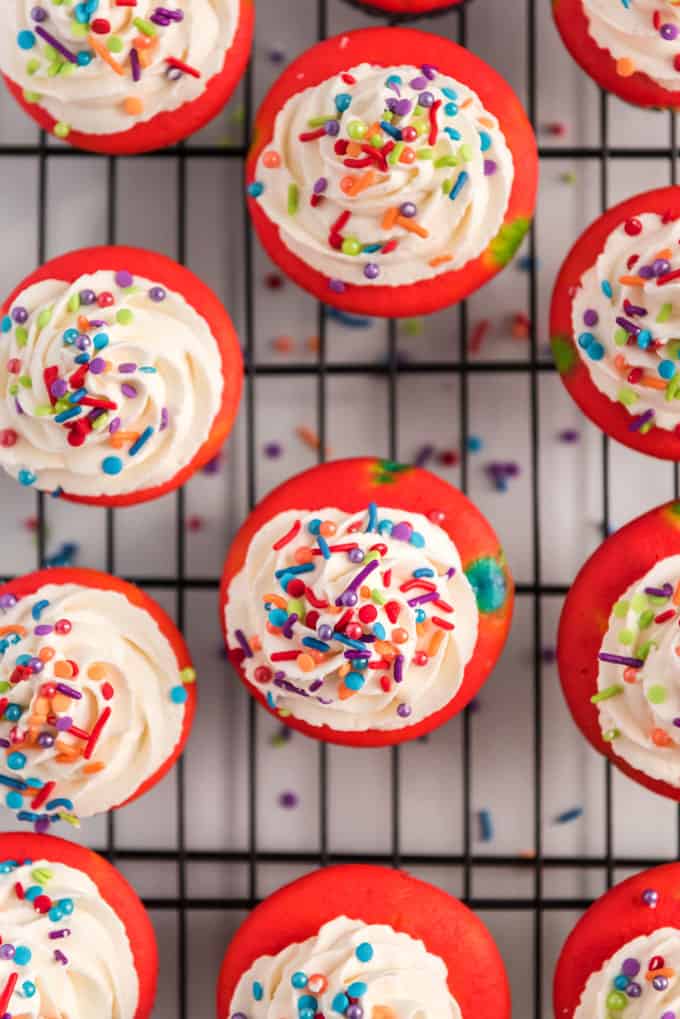 overhead view of colorful rainbow cupcakes with white frosting and sprinkles on cooling rack