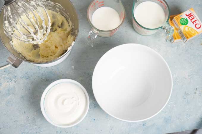 overhead view of stand mixer glass and measuring cups full of milk container whipped cream pudding mix