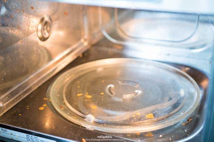 A close up of the inside of a dirty microwave prior to cleaning focusing on the rotating glass plate at the bottom of the microwave