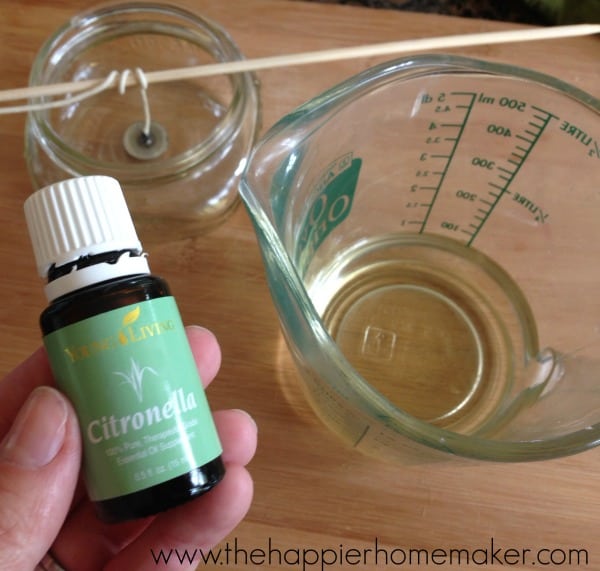 hand holding bottle of citronella oil above measuring cup and mason jar
