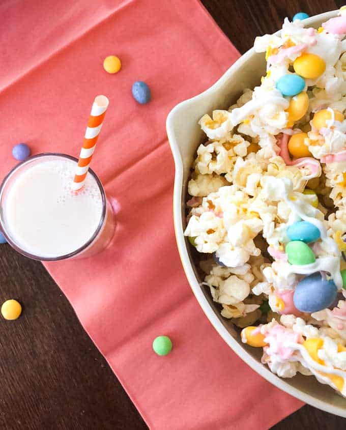 overhead view of bowl of popcorn with pastel candies in it and glass of milk