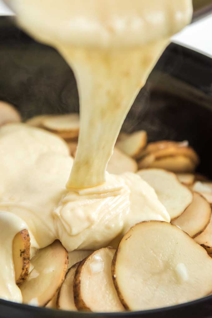 pouring cheese on scalloped potatoes in slow cooker