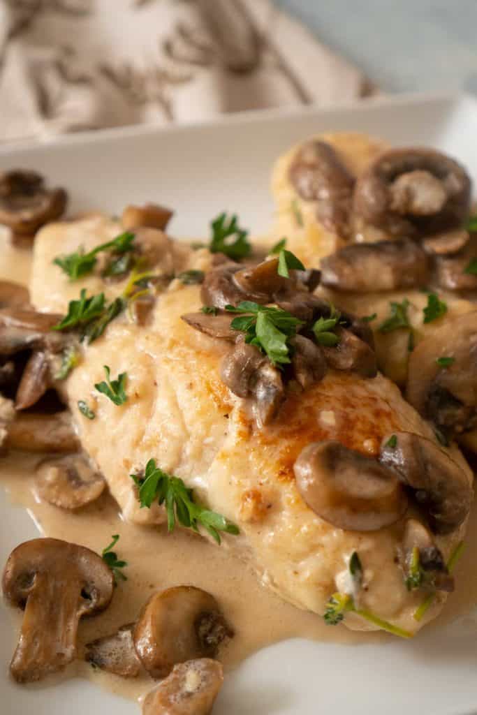 close up of chicken marsala on white plate with mushroom slices and fresh parsley on top
