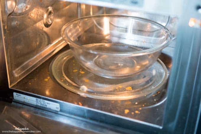 A close up of the inside of a dirty microwave with a bowl of water inside it