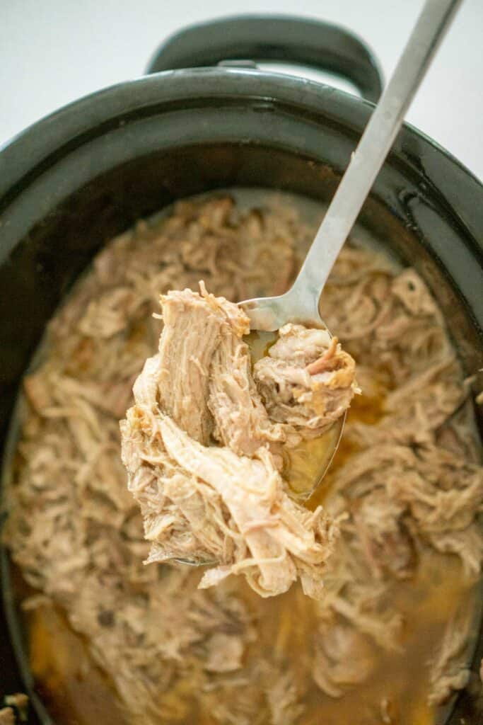 overhead view of pulled pork in slow cooker with spoon scooping some up