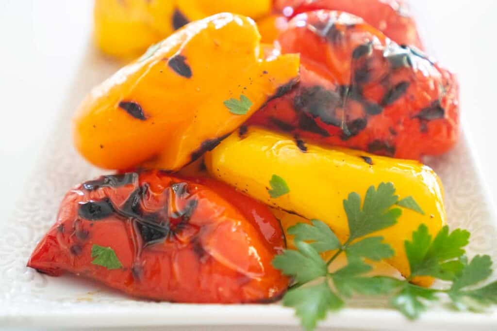 grilled yellow, orange, and red bell peppers on white plate with parsley