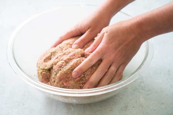 mixing meatloaf in glass bowl with hands