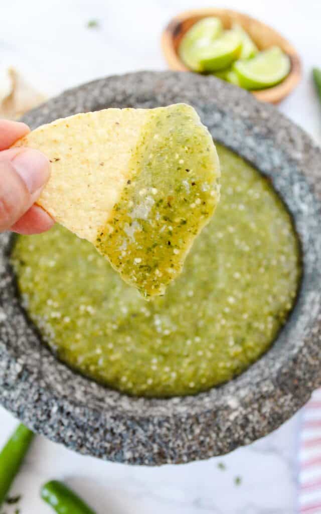 hand holding tortilla chip with salsa verde