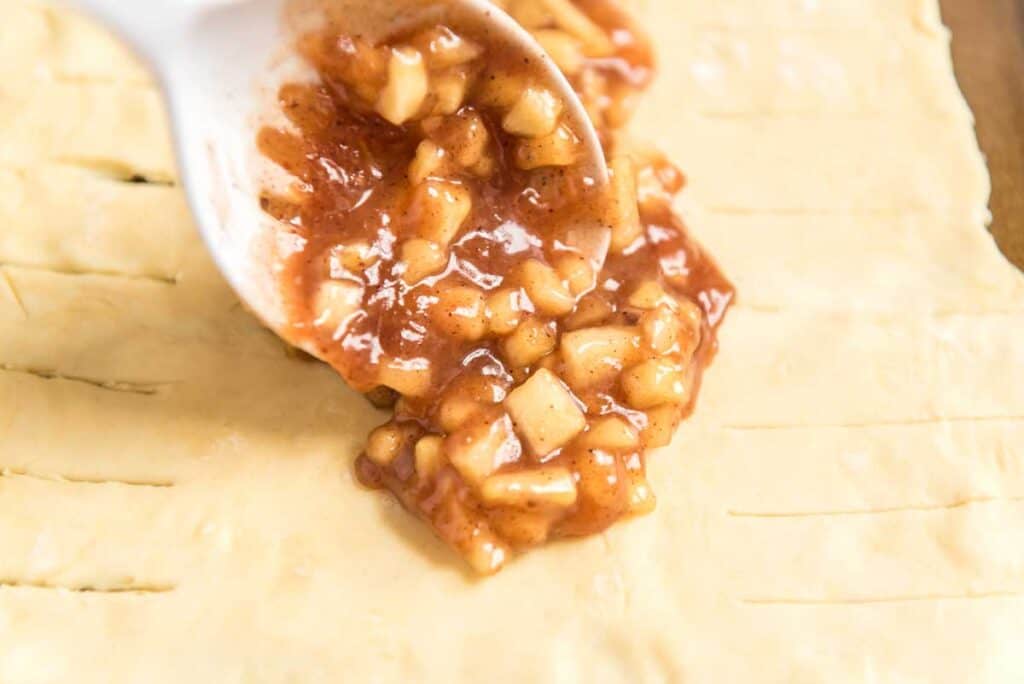 spoon with apple filling pouring on pastry dough