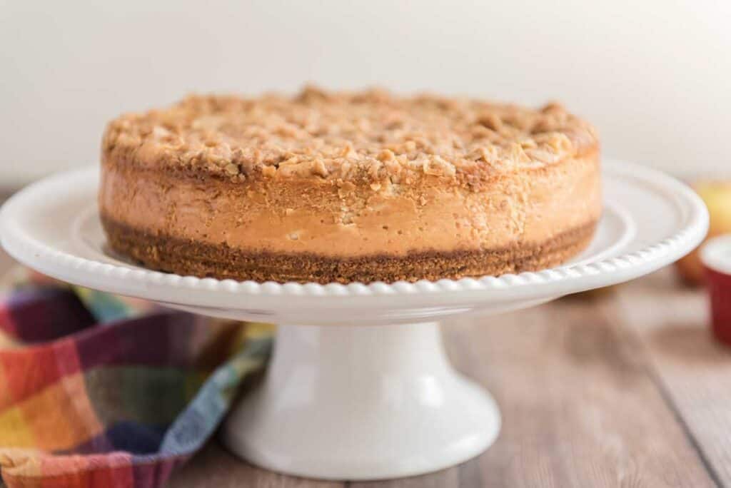 apple crisp cheesecake on white cakestand