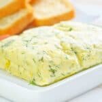 garlic butter with herbs on white tray with bread in background