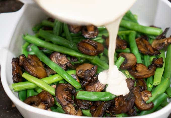 A bowl filled with meat and vegetables, with a white casserole sauce being bored on