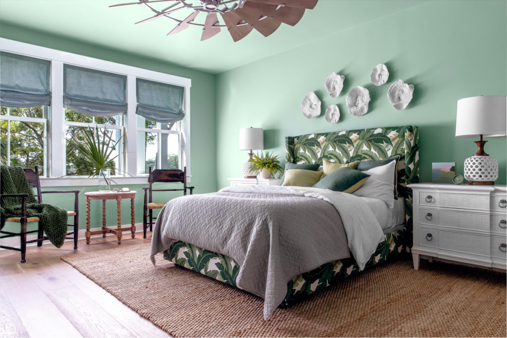 A bedroom with a large bed with palm tree printed headboard and frame with shells on walls and woven jute rug