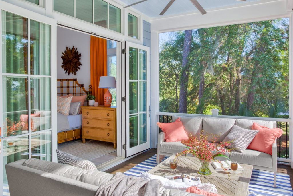 covered screen porch with glass doors leading to bedroom and taupe seating with coral pillows