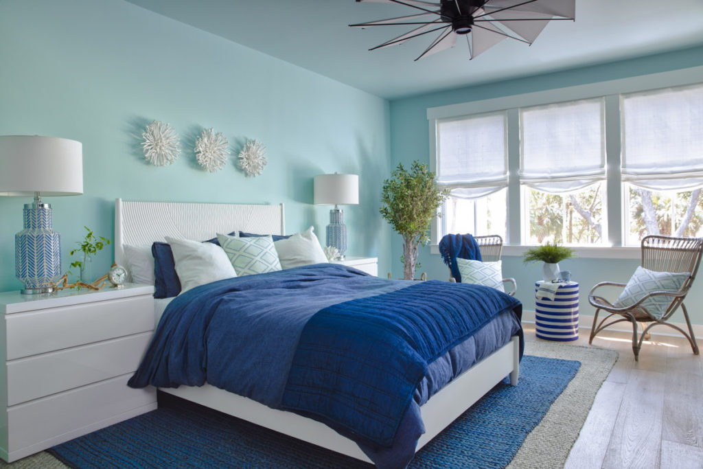 A turquoise walled bedroom with a bed with blue bedding and white headboard and side table 