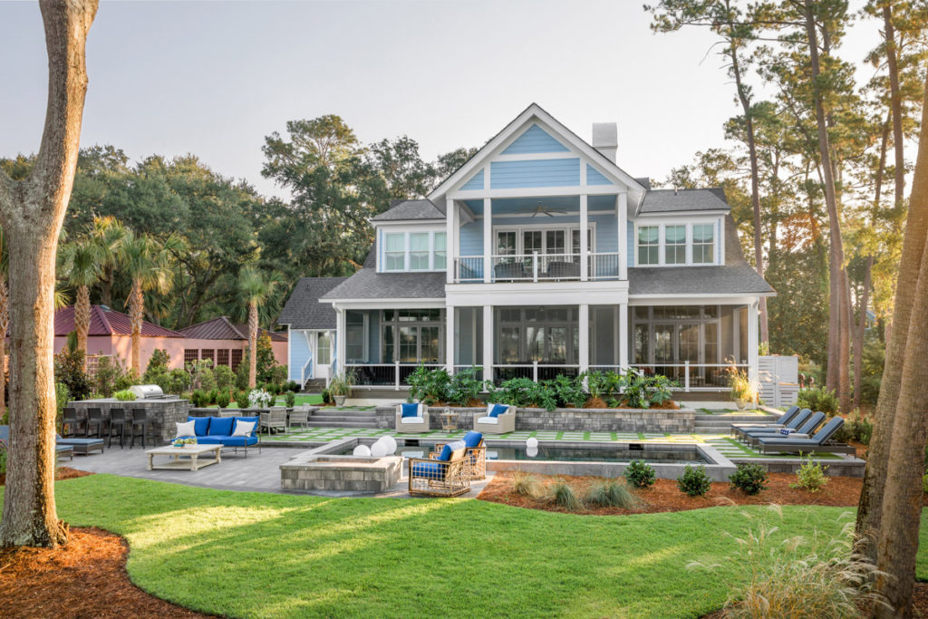 A large lawn with pool and outdoor fire pit behind a blue house that was the hgtv dream home 2020