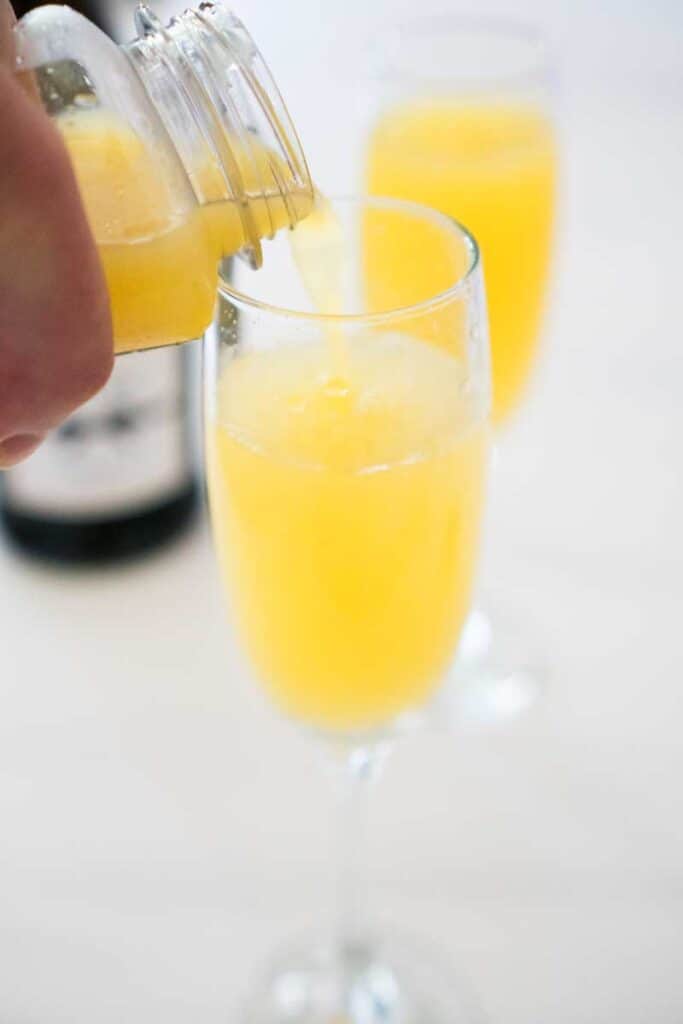 orange juice pouring into champagne flute with processo