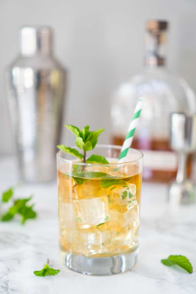 Mint julep in glass with green and white striped straw and mint sprig garnish