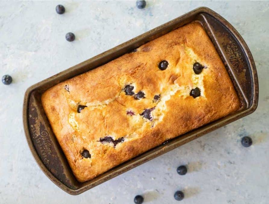 overhead view of blueberry cream cheese bread in a loaf pan with whole blueberries scatttered about