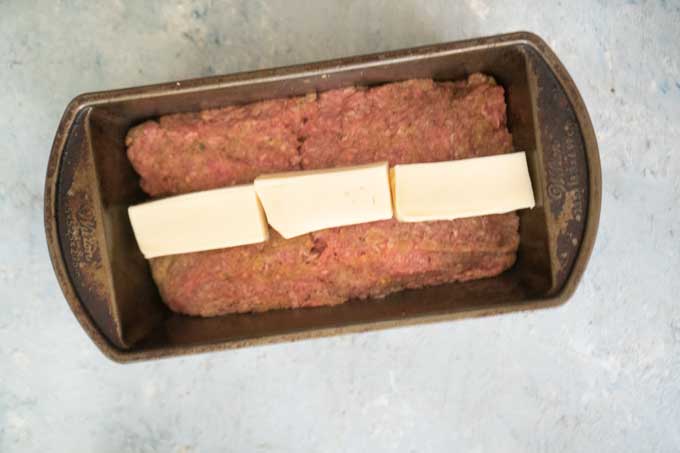 uncooked meatloaf in baking pan with mozzarella cheese on top