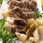 leg of lamb on white platter with potatoes garnished with oregano