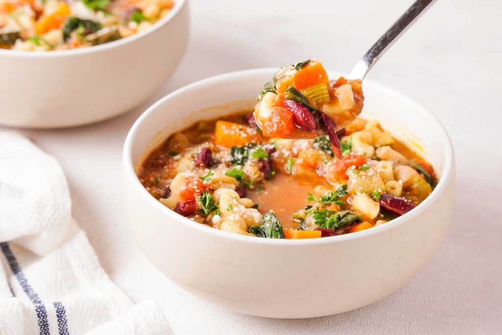 spoon scooping minestrone out of a white bowl