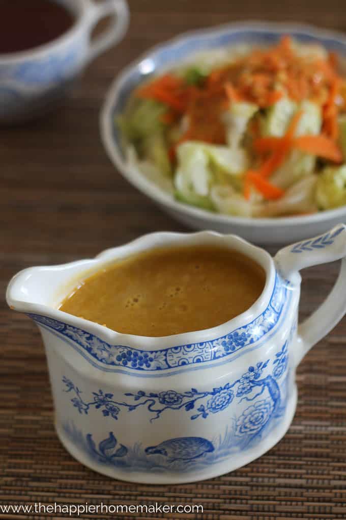 A white and blue gravy cup with ginger dressing in front of a salad