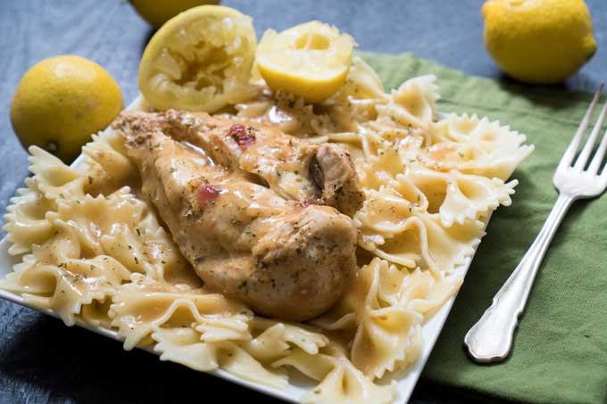 lemon chicken breast on bowtie noodles with squeezed lemons in background