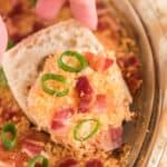 Charleston cheese dip in bowl with green onion and hand holding tortilla chip with dip on it