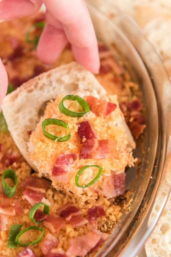 Charleston cheese dip in glass serving dish with hand holding tortilla chip with dip in the foreground