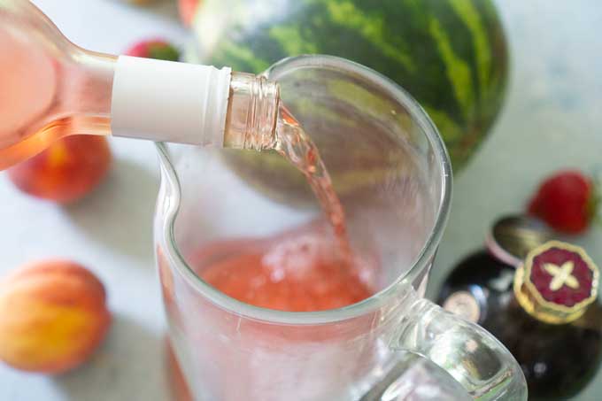 pouring rose wine into glass pitcher 