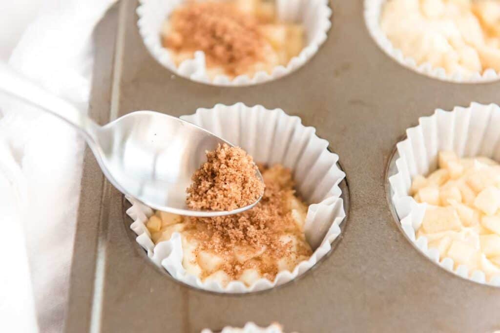 spoon sprinkling cinnamon sugar over muffin batter in tin