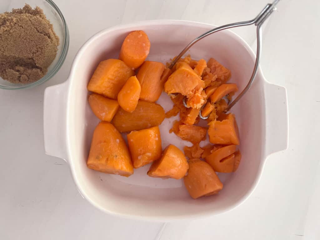 canned yams in baking dish ith potato masher